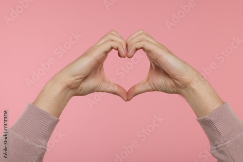 Man showing heart gesture with hands on pink background  closeup