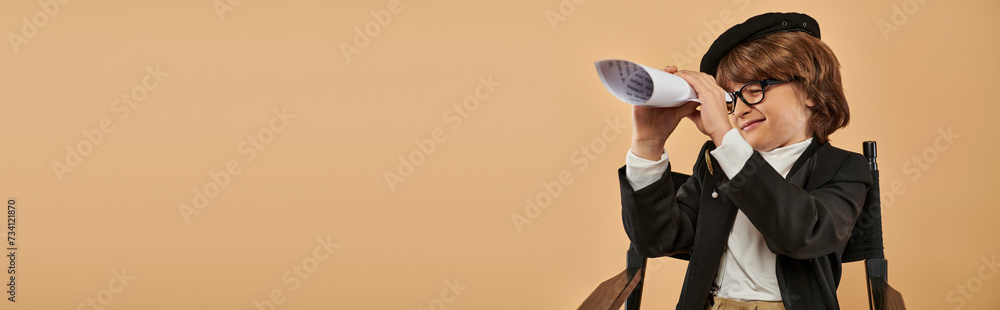 boy in stylish clothing sits on director chair and looking through hole in rolled paper, banner boy in stylish clothing sits on director chair and looking through hole in rolled paper, banner