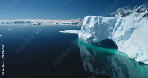 Glacier arch with icicles float melted blue water in sunny day. Open Antarctic ocean coast nature mountain beauty. Pristine Arctic landscape. Antarctica polar summer. Global warming climate change.