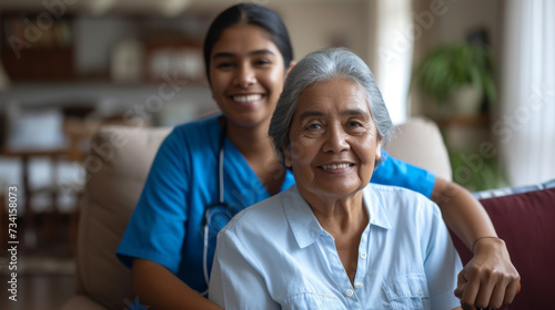 young female nurse in blue scrubs smiling next to a happy elderly woman in a white shirt, likely depicting a caring moment in a healthcare or home setting.