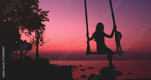 Woman silhouette sway on wooden rope swing against bright pink sunset. Vacation on beautiful seacoast. Travel, tourism, holiday on paradise Thailand Island. Nature landscape in sunrise.