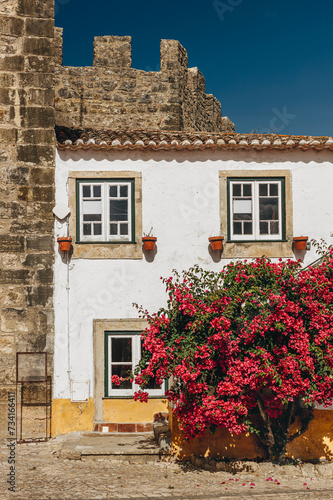 Bbuilding facade with bougainvillea and fragment of the castle walls in Obidos, Portugal.