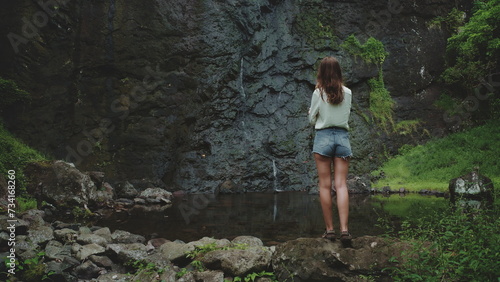 Woman enjoy jungle waterfall standing on rock. Travel to Bali island  Indonesia. Outdoor lifestyle travel on summer holiday vacation. Dark dramatic toning. Back view