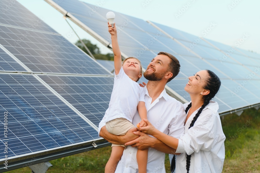 © Serhii - Solar energy concept. A young, happy family is standing near solar panels and holding an electric light bulb.