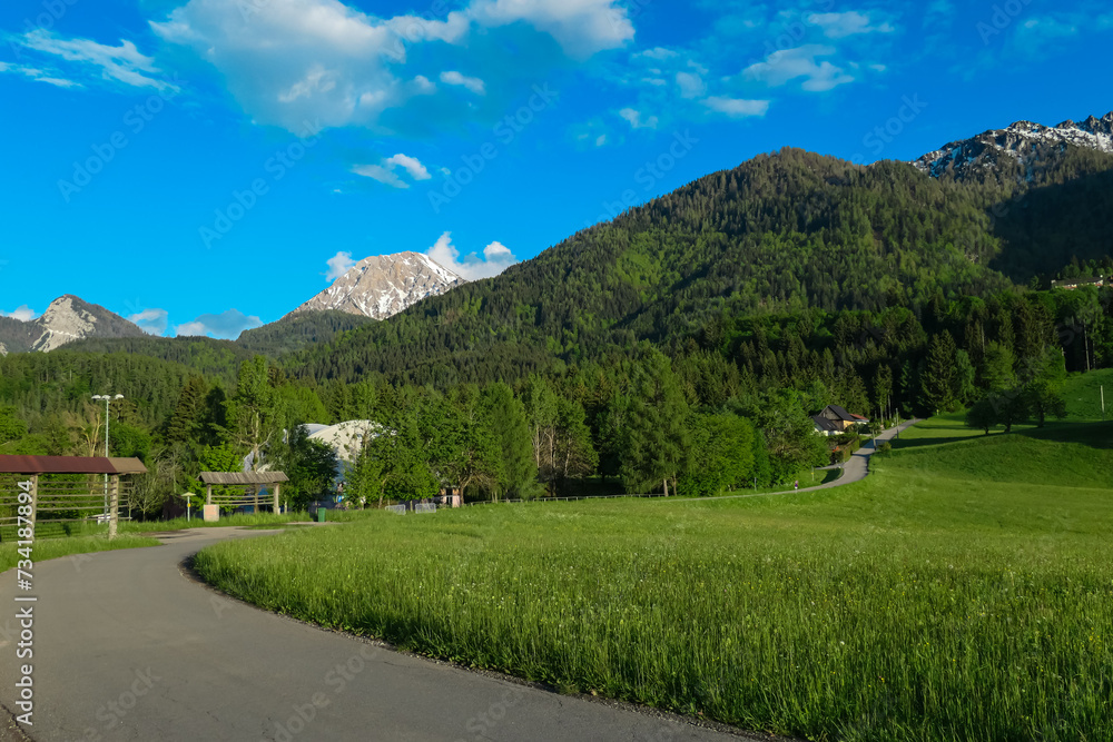 Idyllic alpine road with scenic view of majestic mountain peak Mittagskogel in Karawanks seen from Altfinkenstein at Baumgartnerhoehe, Carinthia, Austria. Tranquility on hiking trail in Austrian Alps