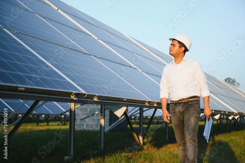 Portrait of Young indian male engineer standing near solar panels, with clear blue sky background, Renewable and clean energy. skill india, copy space