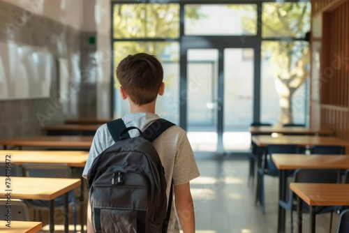 unrecognizeable student boy with backpack walks into classroom