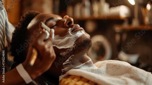 young man reclining in a barber's chair with shaving cream applied to his beard and neck, as a barber is carefully shaving him