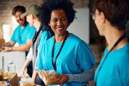 Happy black volunteer talking to her coworker while working at food bank. photo