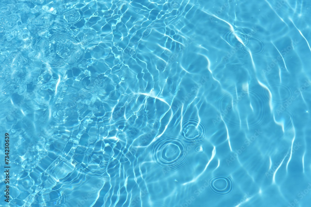 Water surface. Bluewater waves on the surface ripples blurred. Defocus blurred transparent blue colored clear calm water surface texture with splash and bubbles. Water waves with shining pattern.