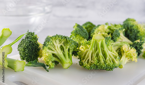Broccoli florets close-up. Fresh raw organic broccoli on a white cutting board on kitchen table, still life, cooking process