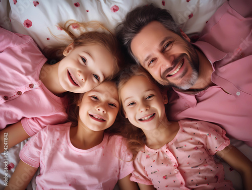 Young happy family or father with daughters lying on bed and having great fun, view from above.Happy family theme 