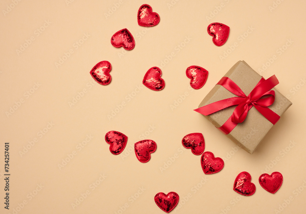 Box tied with a red ribbon and small hearts on a beige background, top view Box tied with a red ribbon and small hearts on a beige background, top view