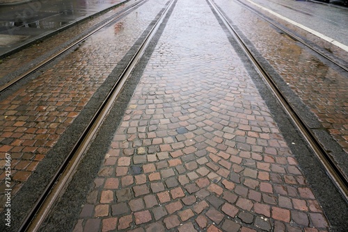 Nasse Straßenbahnschienen zwischen buntem Pflastersteinboden in Großstadt bei Regen am Mittag im Winter