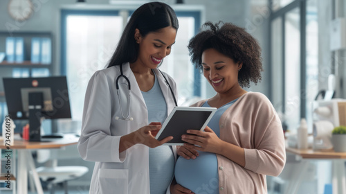 smiling pregnant woman is looking at a tablet screen shown to her by a healthcare professional in a medical office setting.