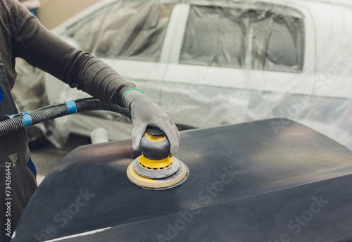 Auto mechanic preparing the car for paint job by applying polish with the power buffer machine photo