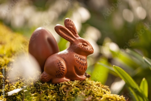 Small chocolate bunny with eggs sitting on green forest