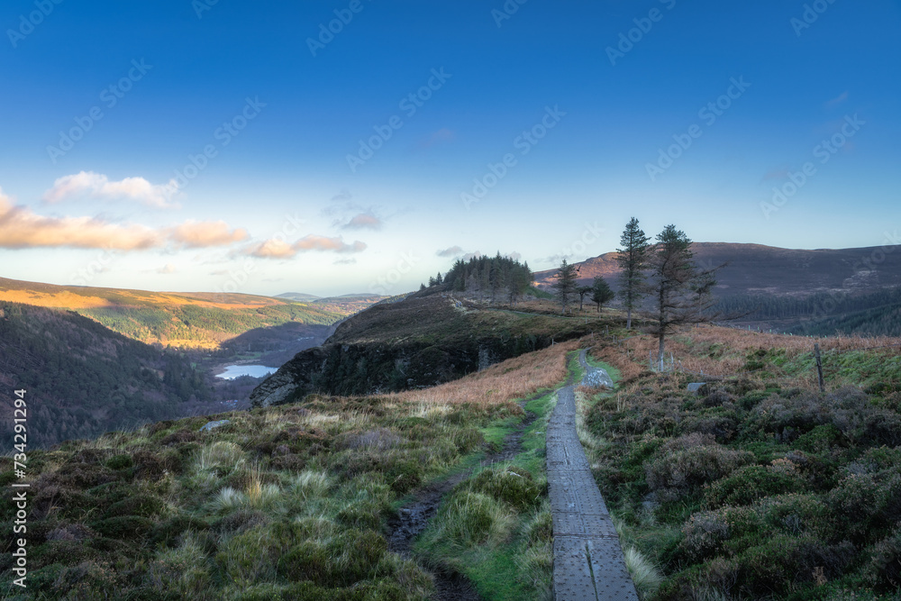 Wooden boardwalk on the top of a mountain with scenic view on Glendalough lakes and forest. Hiking in beautiful autumn Wicklow Mountains, Ireland