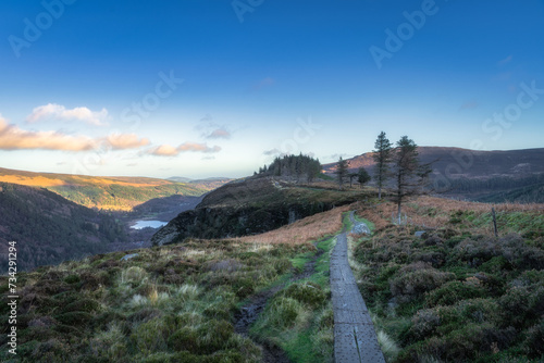 Wooden boardwalk on the top of a mountain with scenic view on Glendalough lakes and forest. Hiking in beautiful autumn Wicklow Mountains  Ireland