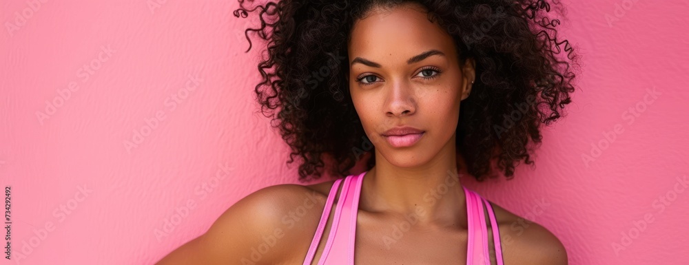 A portrait of a fitness woman striking a pose while wearing a pink tank top against a pink background.