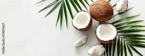 A photo of fresh coconuts, both whole and cut in half, alongside palm leaves, all set against a white background.