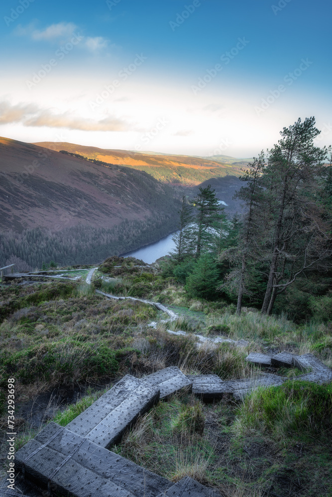 Wooden steps of a boardwalk on the top of a mountain with scenic view on Glendalough lakes and forest. Hiking in Wicklow Mountains, Ireland