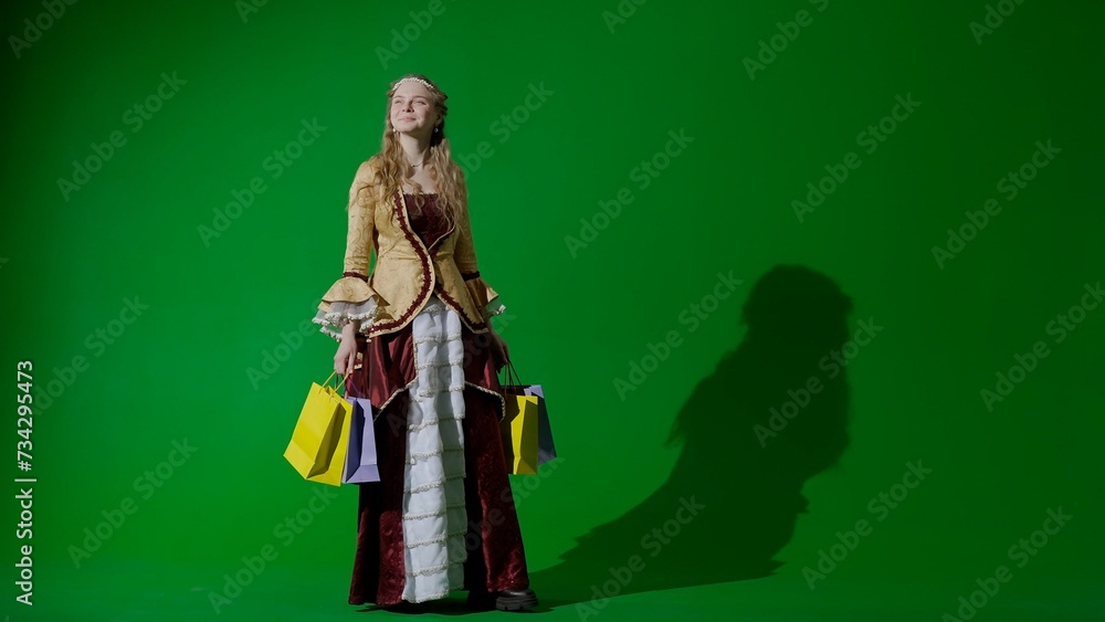 Fototapeta premium Woman in ancient outfit on the chroma key green screen background. Female in renaissance style dress with many shopping gift bags.