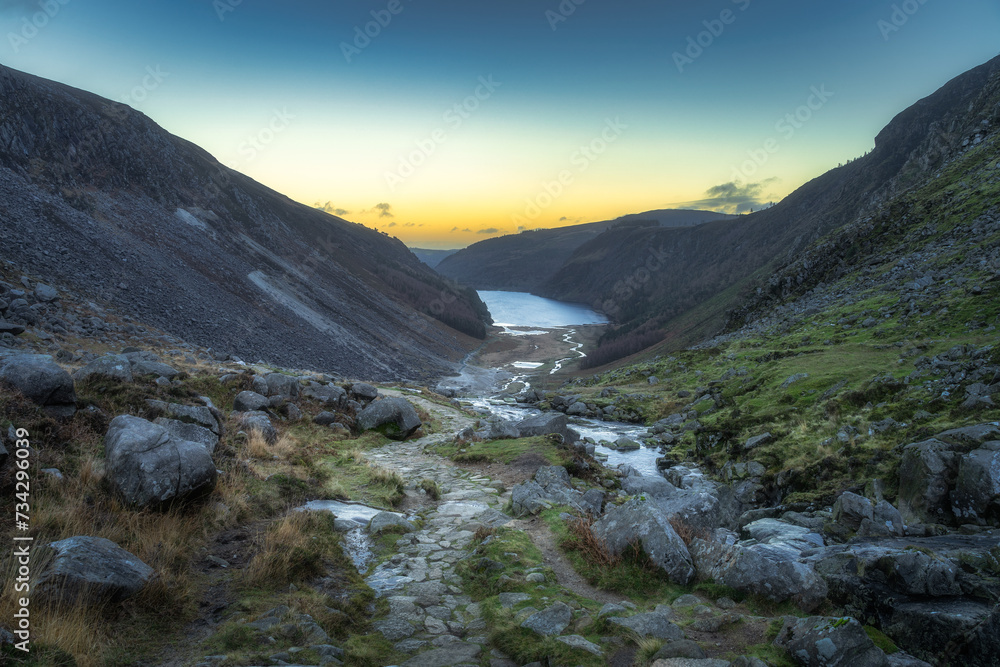 Stone path, trail with a scenic view on Glendalough Lake, stream and valley. Hiking in Wicklow Mountains at sunset, Ireland