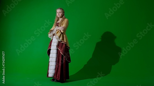Woman in ancient outfit on the chroma key green screen background. Female in renaissance style dress posing looking at the camera, crying sad face.