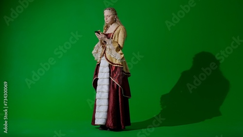 Woman in ancient outfit on the chroma key green screen background. Woman in renaissance style dress texting on her smartphone.