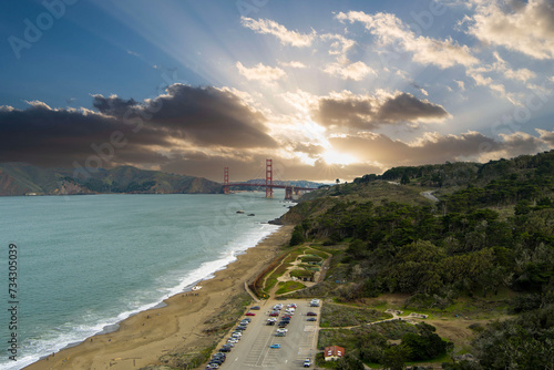 aerial shot of the Golden Gate Bridge and the blue waters of the bay with lush green trees, plants and grass along the hillside and people on the beach in San Francisco California USA