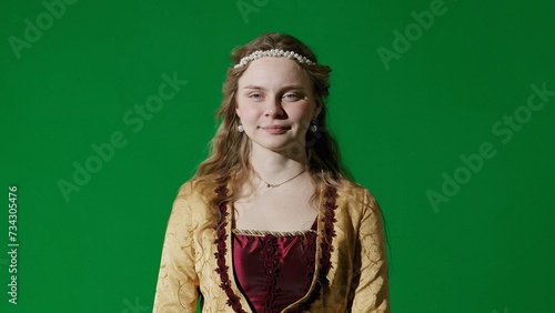 Woman in ancient outfit on the chroma key green screen background. Female in renaissance style dress posing looking at the camera, smiling face. © kinomaster