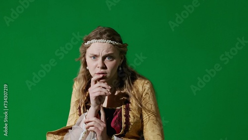 Woman in ancient outfit on chroma key green screen background. Female in renaissance style dress posing looking at the camera, scared shocked face.