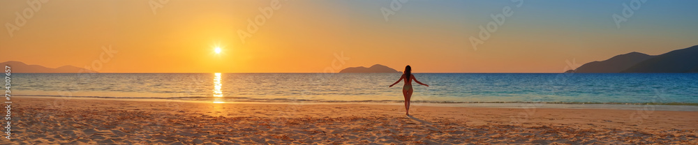 The majesty of nature: a scenic sunset with a woman standing alone on a sandy beach, surrounded by the ocean and mountains in the distance