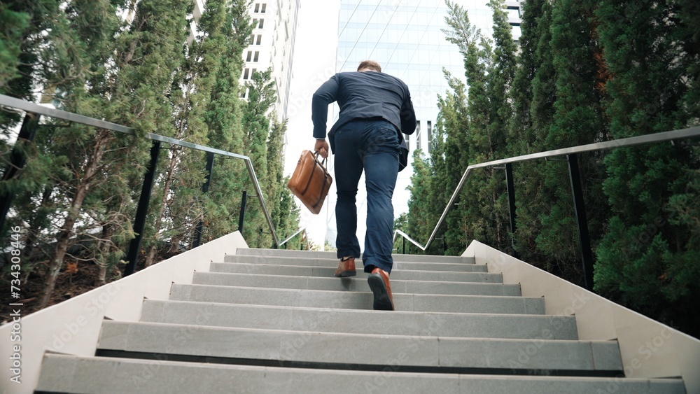 Caucasian businessman walking up stair and calling manager by using smart phone. Back view of manager talking marketing team and planning financial strategy by telephone while going up stair. Urbane.