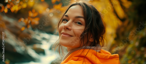 A portrait of a beautiful 34 year old woman looking at the camera being happy, playful, wearing a colored hoodie, radiant, in nature