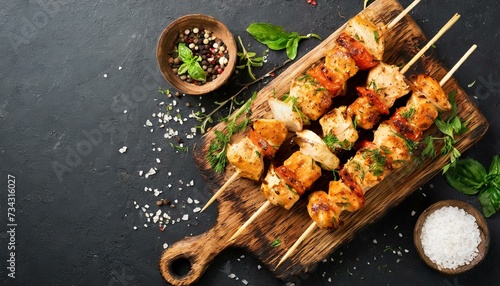 Grilled chicken kebab skewers on a woden cutting board over black slate, stone or concrete background. Top view with copy space. 