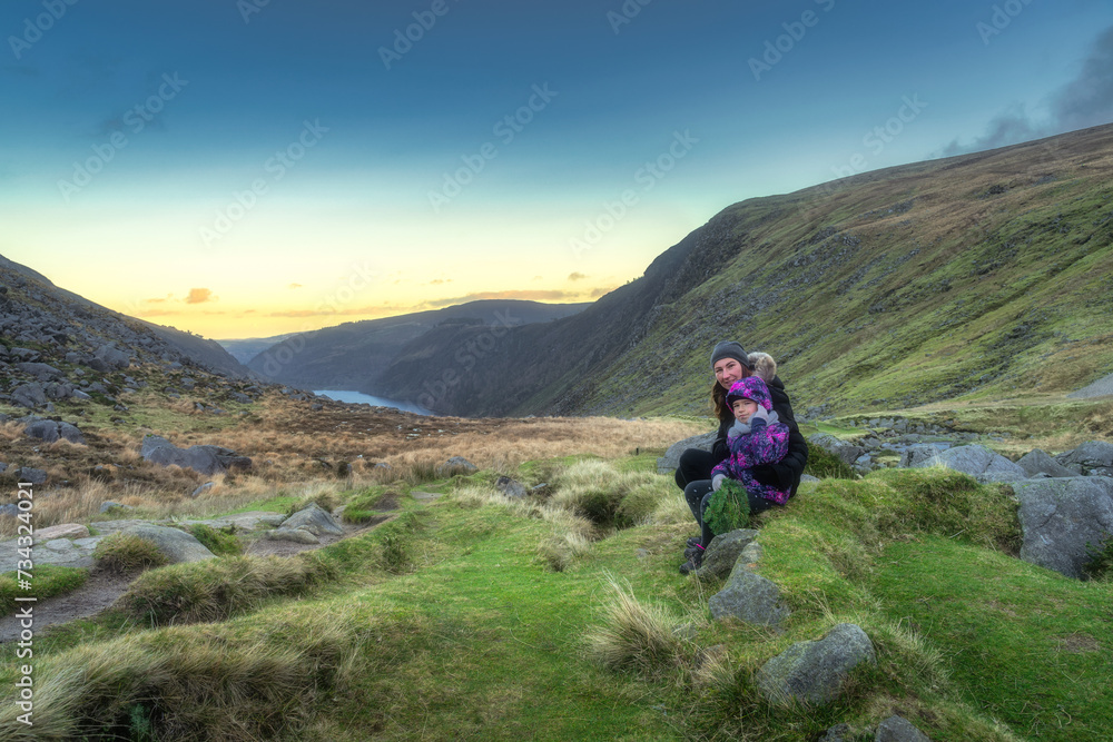 Mother and daughter sitting on a stone in Glendalough at sunset. Hiking in beautiful autumn Wicklow Mountains, Ireland
