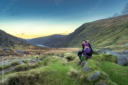 Mother and daughter sitting on a stone in Glendalough at sunset. Hiking in beautiful autumn Wicklow Mountains, Ireland