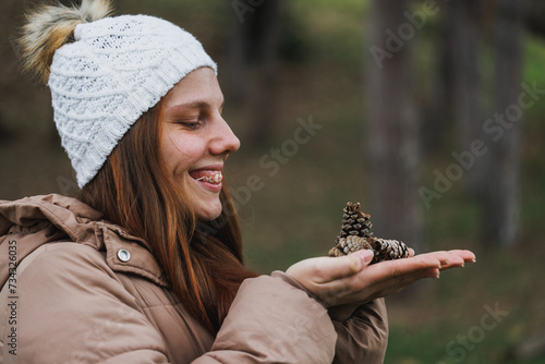 Woman With Braces Holding Pine Cone in Hands Outdoors