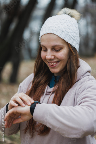 Woman in White Hat Checking Smartwatch During a Winter Run in the Park