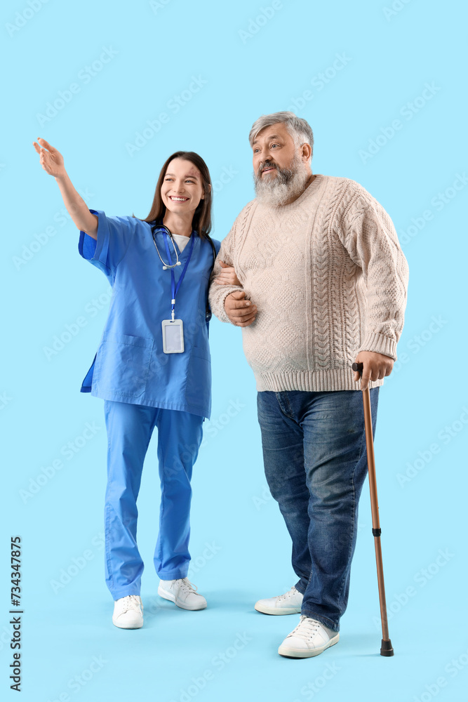 Mature man with walking stick and nurse showing something on blue background Mature man with walking stick and nurse showing something on blue background