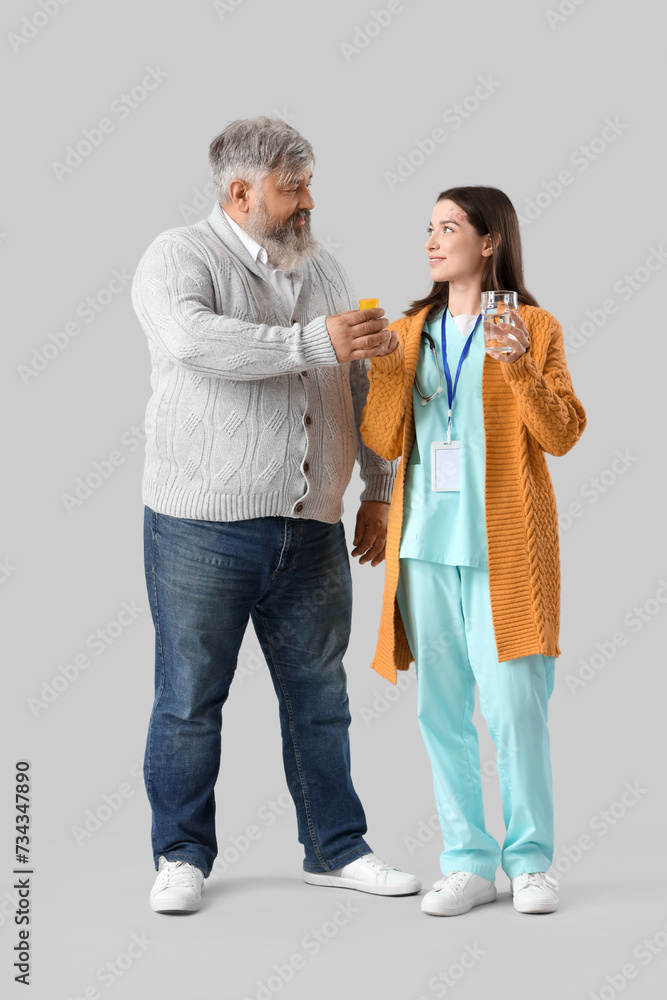 Mature man taking pills and glass of water from nurse on light background