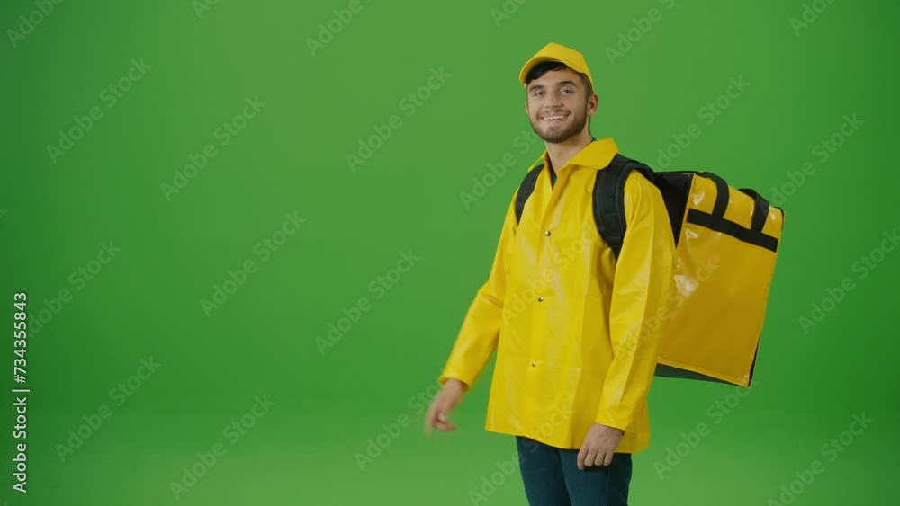 Green Screen Young Food Delivery Person in Yellow Uniform and With a Thermal Backpack and Using Smartphone to Check Order. Courier On the Way to Deliver Order to Client. Back View Green Screen Young Food Delivery Person in Yellow Uniform and With a Thermal Backpack and Using Smartphone to Check Order. Courier On the Way to Deliver Order to Client. Back View