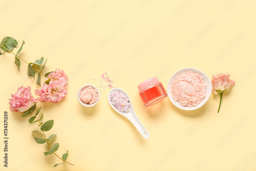 Scrubs with sea salt, cosmetic oil and flowers on light yellow background. Body massage concept
