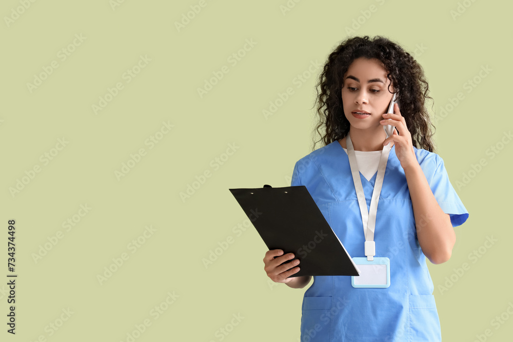 Female African-American medical intern with clipboard talking by mobile phone on green background