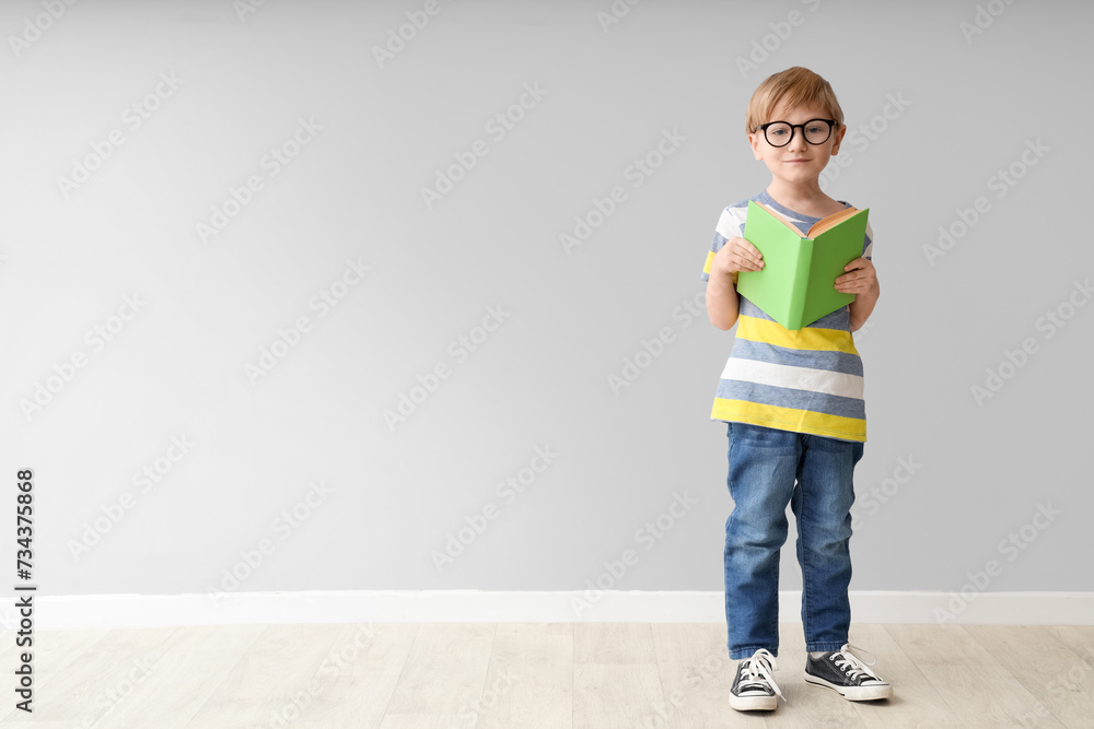 Cute little boy in eyeglasses with open book near grey wall Cute little boy in eyeglasses with open book near grey wall