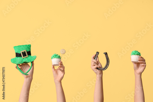 Female hands with tasty cupcakes, leprechaun hat and horseshoe for St. Patrick's Day on beige background