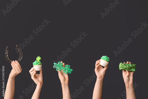 Female hands with tasty cupcake, gift box and horseshoe for St. Patrick's Day on black background