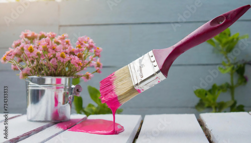 paintbrush with pink paint on wooden table with flowers in background photo